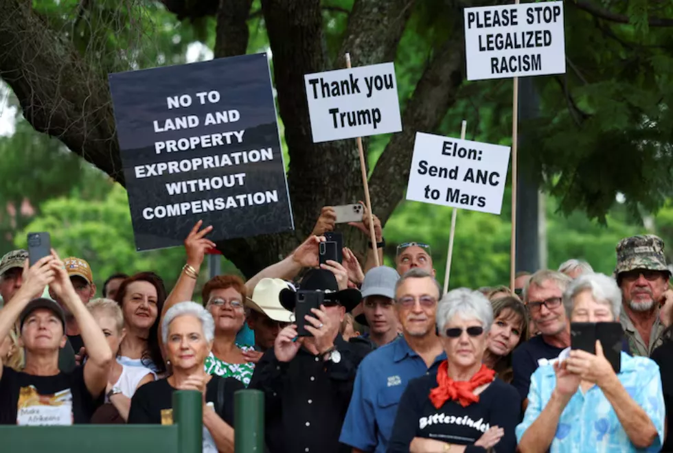 Manifestantes seguram cartazes em apoio à posição do presidente dos EUA, Donald Trump, contra o que ele chama de leis racistas, expropriação de terras e ataques a fazendas, em frente à Embaixada Americana em Pretória, África do Sul, em 15 de fevereiro de 2025.
