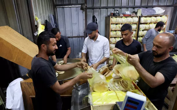 Trabalhadores palestinos embalam pão em uma padaria que voltou a operar após ser fechada devido à escassez de farinha, em Deir Al-Balah, no centro da Faixa de Gaza, em 22 de maio de 2025