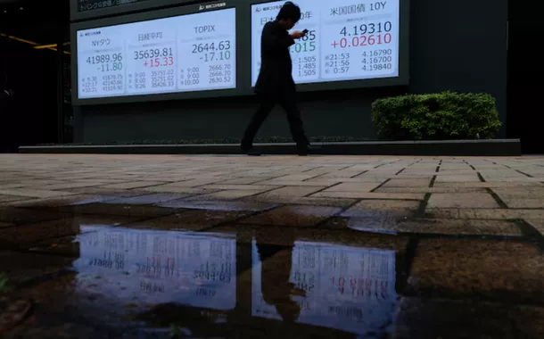 Um homem passa por um painel de cotações de ações mostrando o Índice Industrial Dow Jones, o Índice de Ações Nikkei, o Índice Topix e o rendimento dos títulos do governo japonês e americano de 10 anos, do lado de fora de uma corretora em Tóquio, Japão, em 2 de abril de 2025