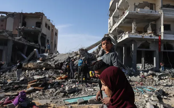 Palestinos deslocados retornam para suas casas enquanto caminham perto de casas destruídas em um ataque israelense durante o conflito, em meio à trégua temporária entre o Hamas e Israel, em Khan Younis, no sul da Faixa de Gaza