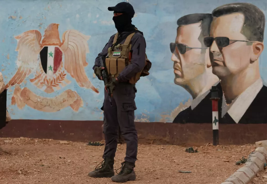 Membro do antigo grupo rebelde Hayat Tahrir al-Sham monta guarda perto de uma imagem de Bashar al-Assad da Síria na sede da quarta divisão em Damasco, Síria, 23 de janeiro de 2025