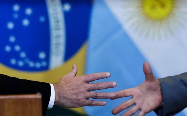 Aperto de mãos em frente às bandeiras do Brasil e da Argentina