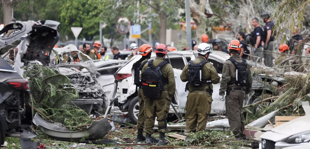 Equipes de resgate trabalham ao lado de veículos danificados em um local atingido por um ataque de mísseis do Irã contra Israel, em Rishon LeZion, Israel, em 14 de junho
