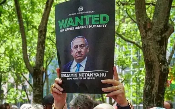 Uma mulher segura um cartaz onde se lê "Procurado por crimes contra a humanidade, Benjamin Netanyahu", durante a manifestação "Red Line For Gaza", em 15 de junho de 2025, em Bruxelas, Bélgica.