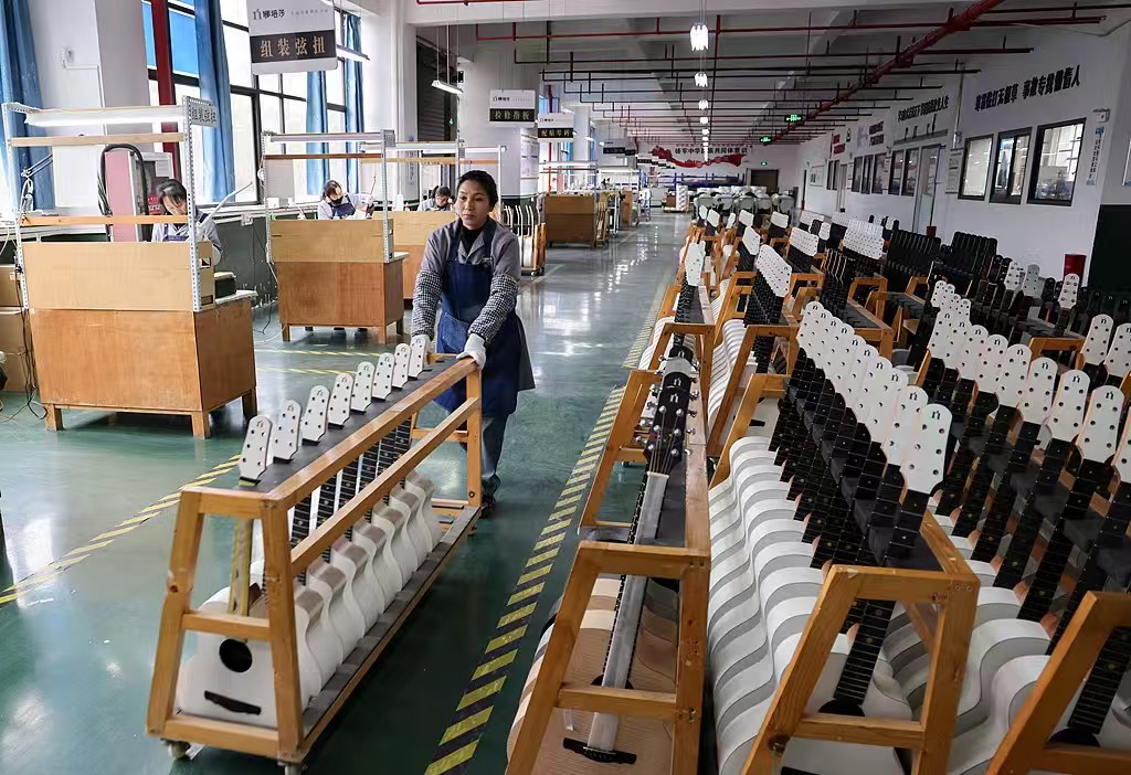 Trabalhador movimenta uma bandeja de guitarras dentro de uma fábrica em Zheng’an, 18 de fevereiro de 2025