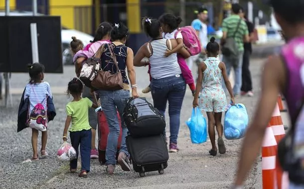 Mulheres e crianças em mudança carregam malas e sacolas