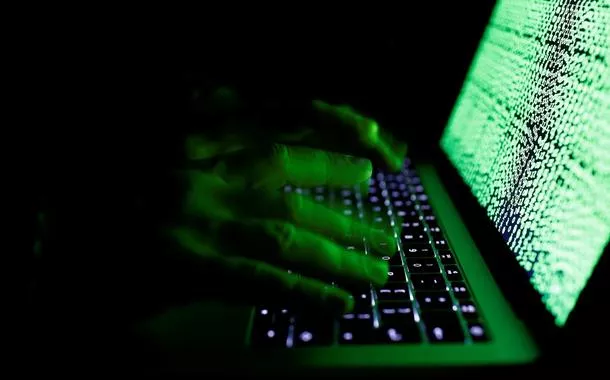 Um homem digita em um teclado de computador em frente a um código cibernético
