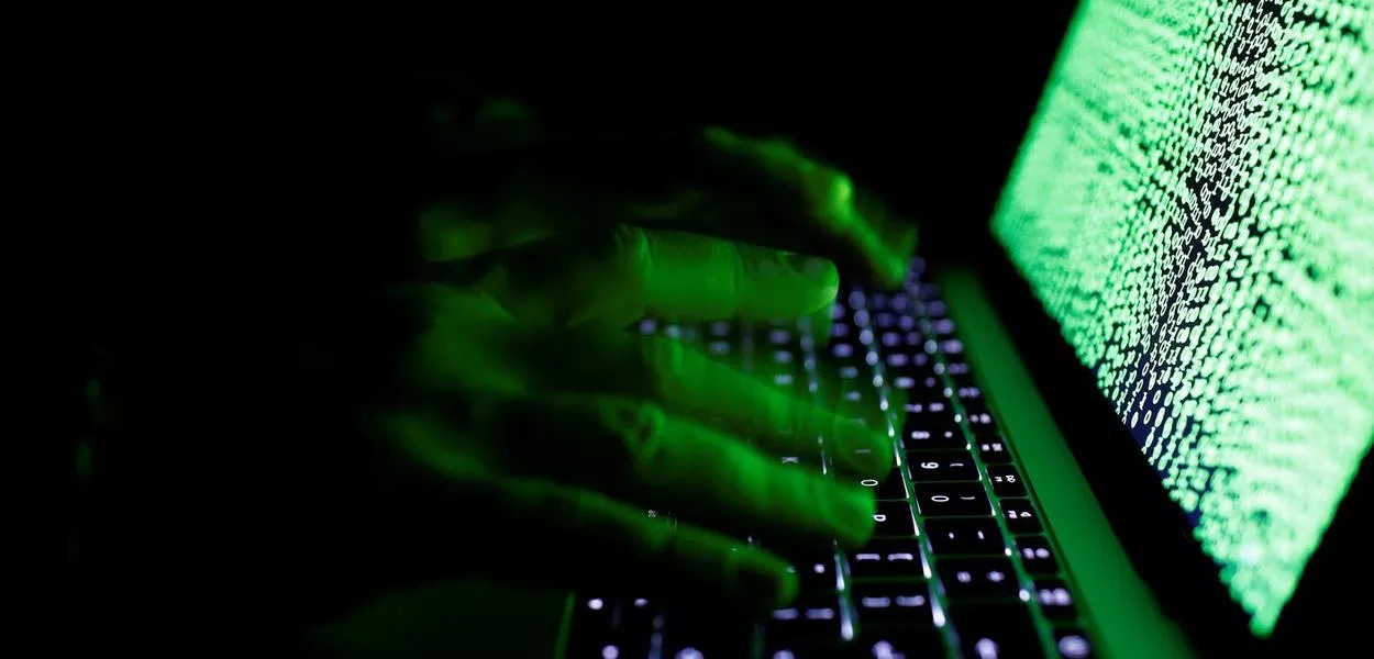 Um homem digita em um teclado de computador em frente a um código cibernético