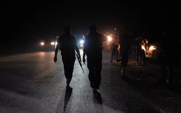 Membros das forças de segurança sírias caminham por uma estrada na zona rural de Sweida, enquanto veículos transportando outras forças de segurança sírias saem da cidade predominantemente drusa de Sweida, Síria, em 16 de julho de 2025