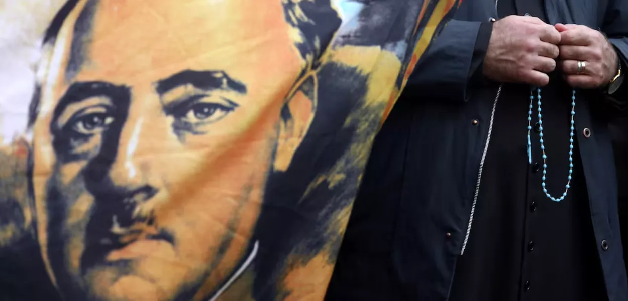 Um padre segura um rosário ao lado de uma bandeira com o retrato do falecido ditador espanhol Francisco Franco, do lado de fora do cemitério Mingorrubio-El Pardo, em Madri, Espanha, em 24 de outubro de 2019