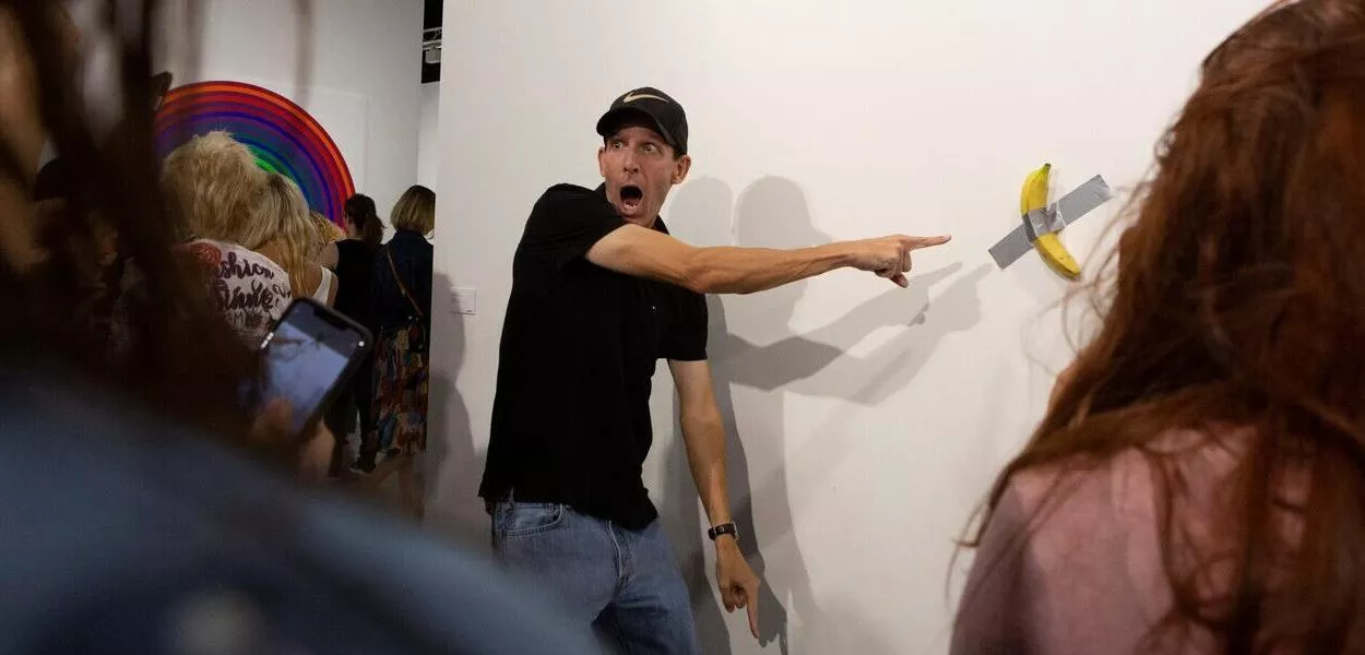Homem posa para foto ao lado da obra "Comedian", de Maurizio Cattelan