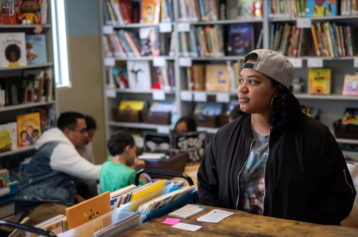 Maria Castro, que tem alguns de seus filhos matriculados no programa de educação infantil Head Start para americanos de baixa renda, posa para um retrato enquanto seu parceiro e os filhos leem livros na biblioteca Educare em Chicago, Illinois, EUA, 19 de maio de 2025