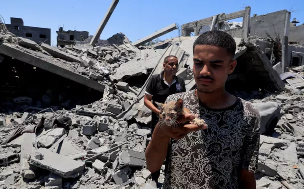 Um palestino segura um gato enquanto inspeciona casas destruídas durante uma operação militar israelense, em Deir al-Balah, no centro da Faixa de Gaza, em 23 de julho de 2025