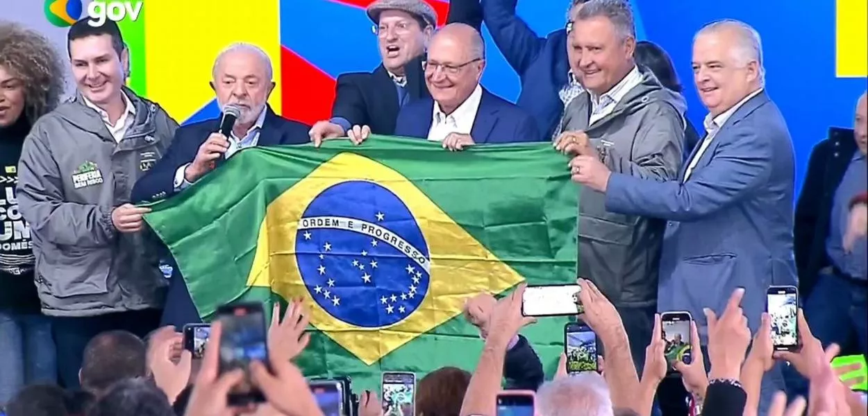 O presidente Luiz Inácio Lula da Silva, com o vice-presidente Geraldo Alckmin, seguram uma bandeira do Brasil, com ministros e outras figuras políticas, em Osasco, SP - 25/07/2025 