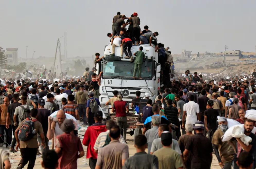 Palestinos correm para recolher suprimentos de ajuda de caminhões que entraram por Israel, em Khan Younis, sul da Faixa de Gaza, 12 de agosto de 2025
