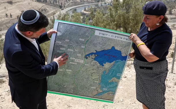 O Ministro das Finanças israelense, Bezalel Smotrich, e uma mulher seguram um mapa que mostra o esquema de assentamento E1, congelado há muito tempo, que separaria Jerusalém Oriental da Cisjordânia ocupada, no dia de uma coletiva de imprensa perto do assentamento israelense de Maale Adumim, na Cisjordânia ocupada por Israel, em 14 de agosto de 2025