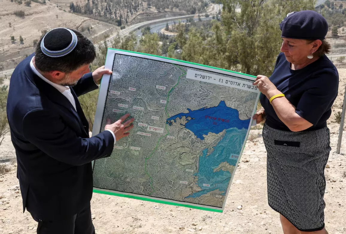 O Ministro das Finanças israelense, Bezalel Smotrich, e uma mulher seguram um mapa que mostra o esquema de assentamento E1, congelado há muito tempo, que separaria Jerusalém Oriental da Cisjordânia ocupada, no dia de uma coletiva de imprensa perto do assentamento israelense de Maale Adumim, na Cisjordânia ocupada por Israel, em 14 de agosto de 2025