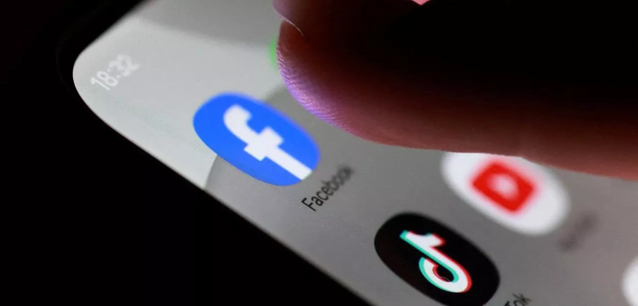 Ilustração com ícones dos aplicativos Facebook, TikTok e YouTube em um smartphone - 27 de outubro de 2025