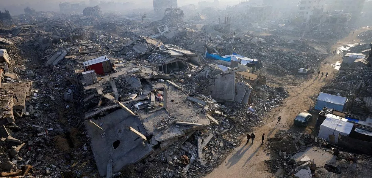 Palestinos caminham em meio aos escombros de prédios destruídos, na Cidade de Gaza - 19/11/2025