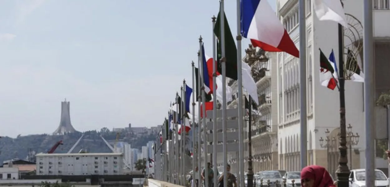 Uma mulher permanece próxima às bandeiras da Argélia e da França antes da chegada do presidente francês, Emmanuel Macron, a Argel para uma visita oficial, em 25 de agosto de 2022