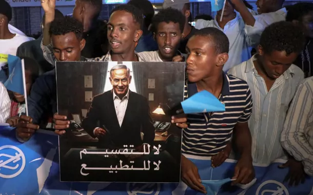 Um manifestante segura uma imagem que retrata o primeiro-ministro israelense, Benjamin Netanyahu, enquanto somalis participam de uma manifestação após Israel se tornar o primeiro país a reconhecer formalmente a autoproclamada República da Somalilândia como um estado independente e soberano, uma decisão que pode remodelar a dinâmica regional e testar a longa oposição da Somália à secessão, no distrito de Hodan, em Mogadíscio, Somália, 28 de dezembro de 2025