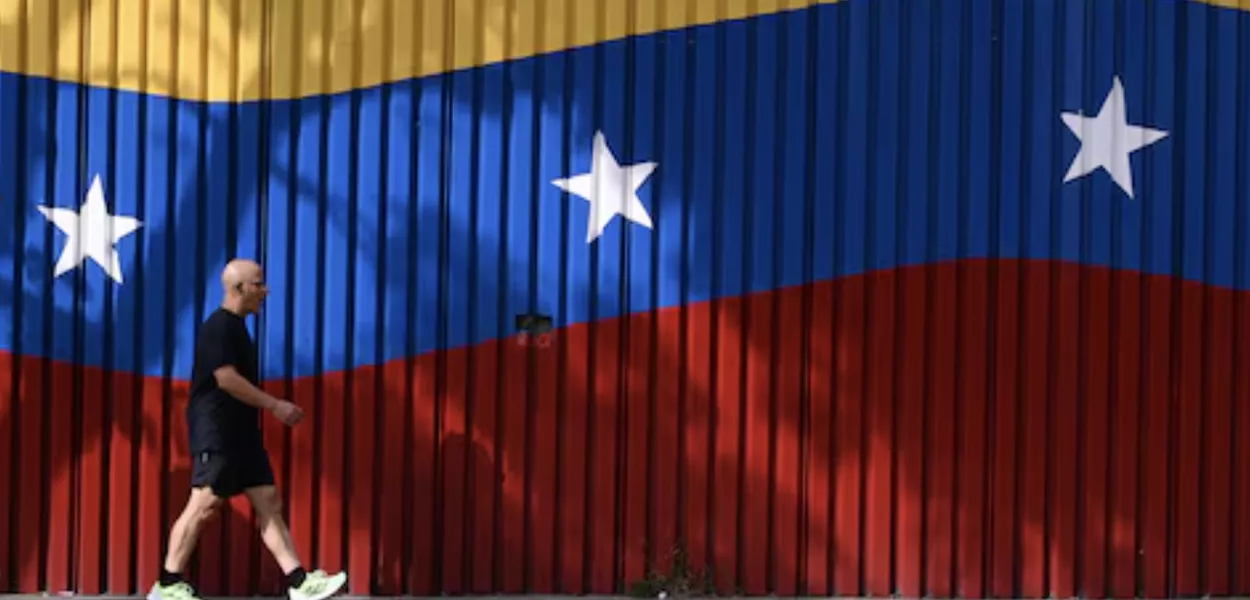 Um homem caminha ao lado de um mural com as cores da bandeira venezuelana, em Caracas, Venezuela - 29 de novembro de 2025