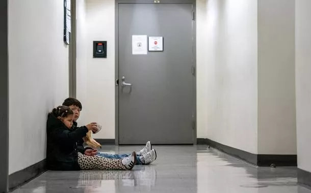 Duas crianças sentam-se no corredor enquanto seus pais participam de uma audiência de imigração no tribunal de imigração dos Estados Unidos, em Manhattan, na cidade de Nova York, em 24 de outubro de 2025
