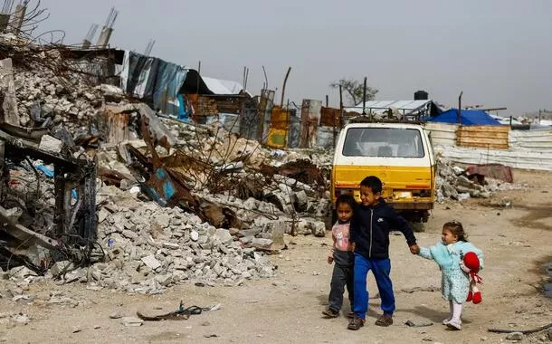 Crianças palestinas caminham entre os escombros de prédios residenciais destruídos na Cidade de Gaza, em 28 de janeiro de 2026
