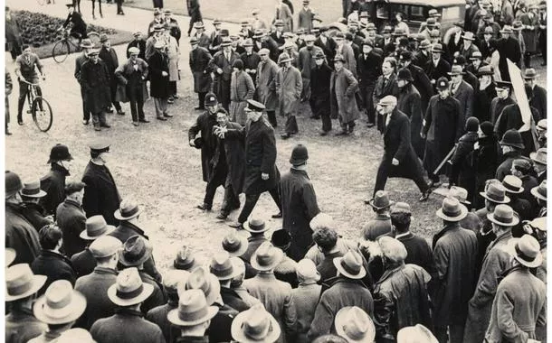 Polícia detém manifestante durante ato do Movimento dos Trabalhadores Desempregados (Unemployed Workers’ Movement) diante do Parlamento da Nova Zelândia, em 1931, em meio à crise social provocada pela Grande Depressão. Foto: Archives New Zealand — Unemployed Workers’ Movement protest, Wellington, 1931 (ADMO 21007 W5985).