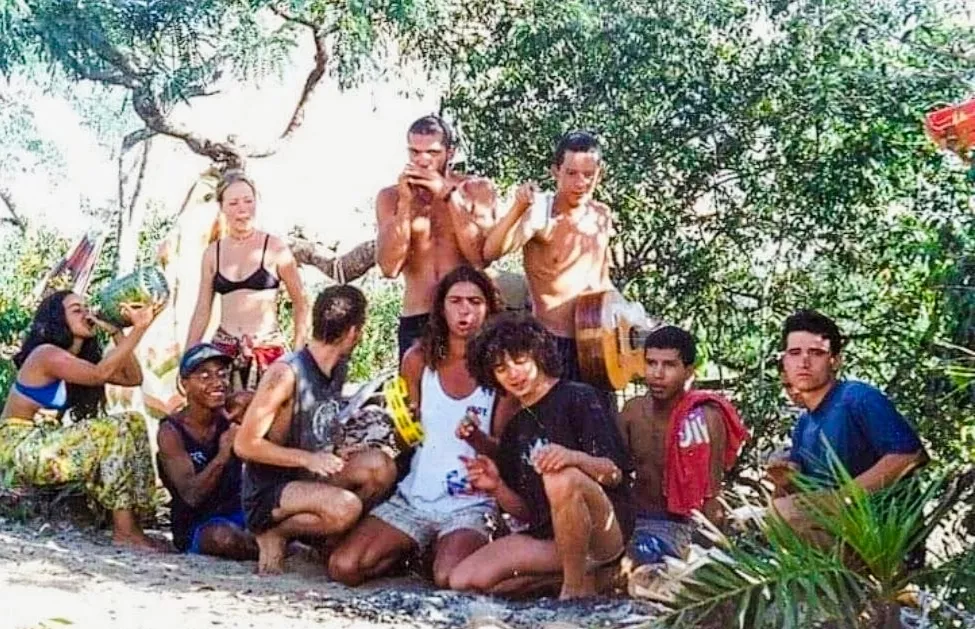 Lelê tocando pandeiro amarelo tendo ao seu lado, de camiseta preta, o punkito.