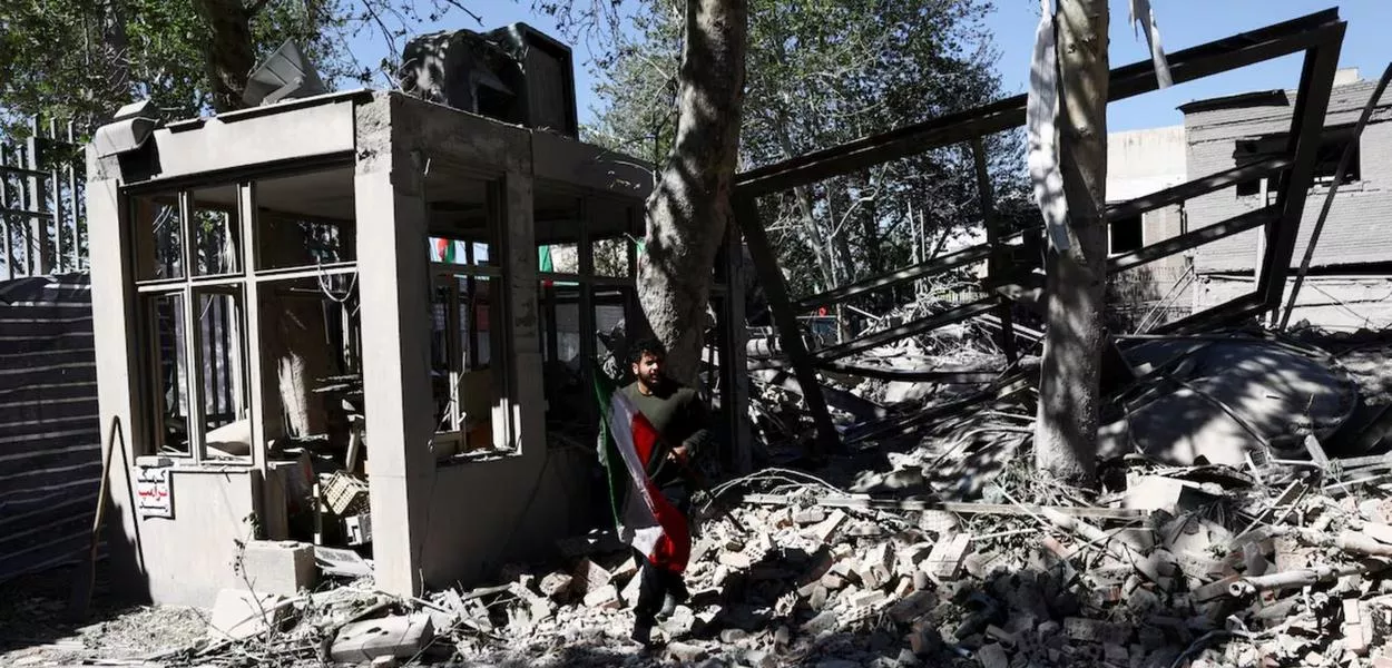 Um homem carrega uma bandeira do Irã enquanto caminha entre os escombros de um prédio da Universidade de Tecnologia Sharif, em Teerã, Irã, em 7 de abril de 2026