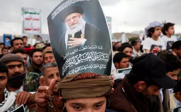 Um manifestante com um cartaz sobre a cabeça exibindo a imagem de Ali Khamenei, participa de uma manifestação com apoiadores houthis em solidariedade ao Irã e ao Líbano
