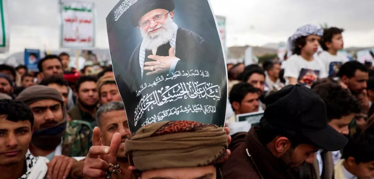 Um manifestante com um cartaz sobre a cabeça exibindo a imagem de Ali Khamenei, participa de uma manifestação com apoiadores houthis em solidariedade ao Irã e ao Líbano