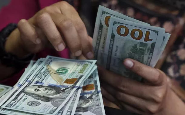 Pessoa conta notas de dólar americano em uma casa de câmbio em Jacarta, Indonésia, em 9 de abril de 2025. Foto tirada através de um vidro
