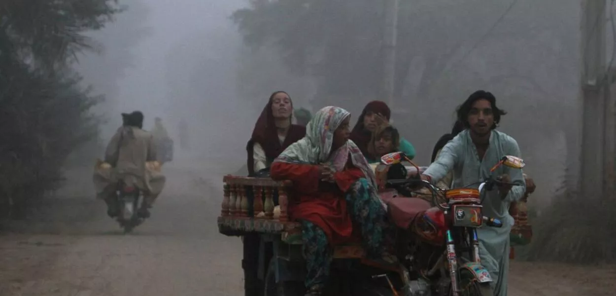 Uma família se desloca em um triciclo motorizado por uma estrada em uma manhã com forte neblina de poluição (smog) nos arredores de Multan, no Paquistão