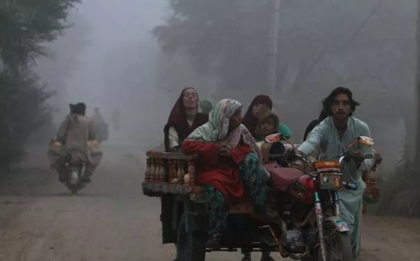 Uma família se desloca em um triciclo motorizado por uma estrada em uma manhã com forte neblina de poluição (smog) nos arredores de Multan, no Paquistão