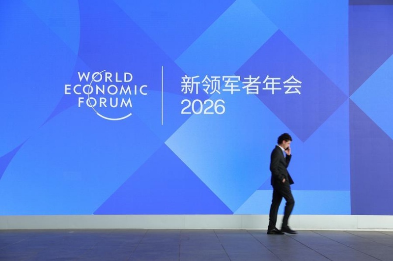 Um participante passa por um outdoor durante o 17º Encontro Anual dos Novos Campeões em Dalian, província de Liaoning, nordeste da China, em 23 de junho de 2026